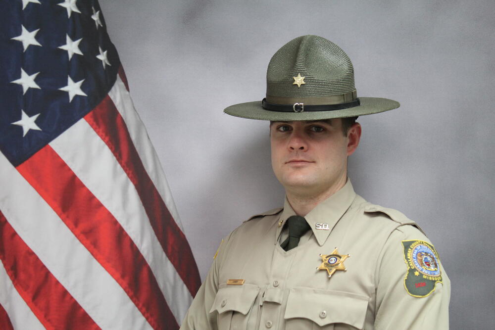 Image of Deputy Zach Carey in uniform pictured in front of an American flag.